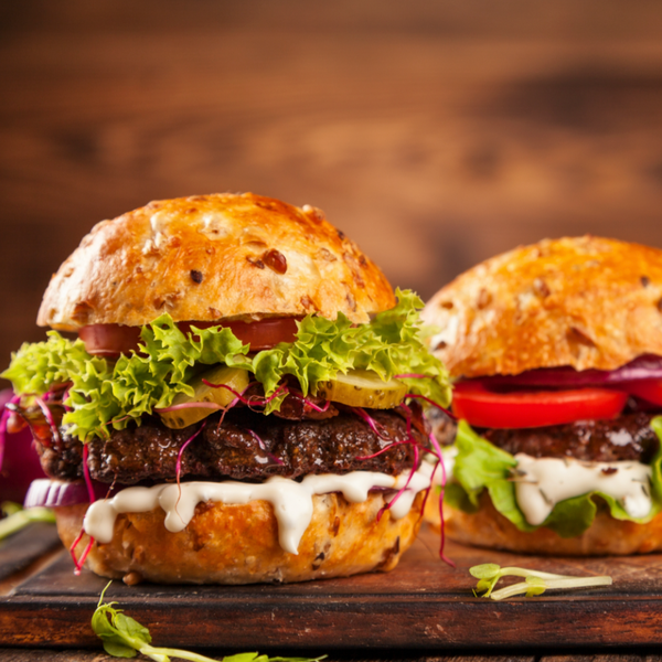 Two hamburgers with lettuce, tomato, onions, and a creamy sauce, on a wooden surface.