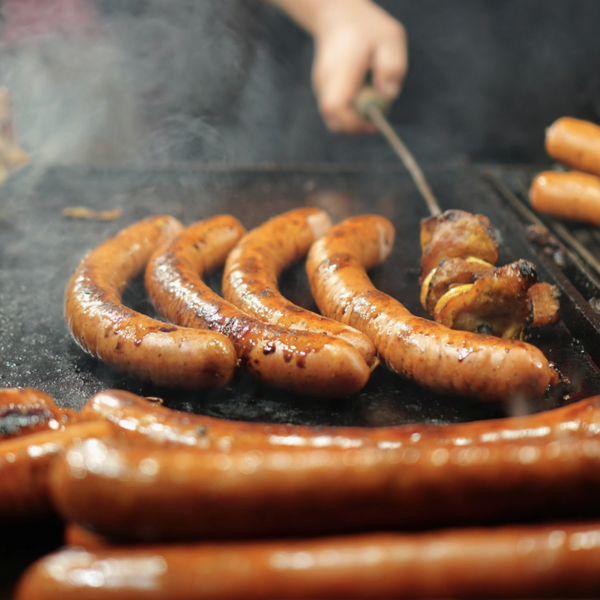 Hot dogs being grilled on a barbecue with smoke in the background