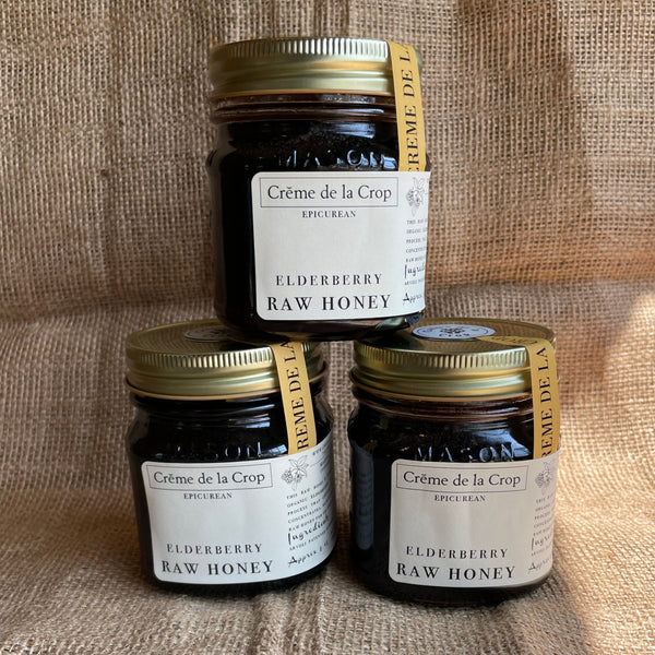 Three jars of Crème de la Crop elderberry raw honey displayed against a burlap background.