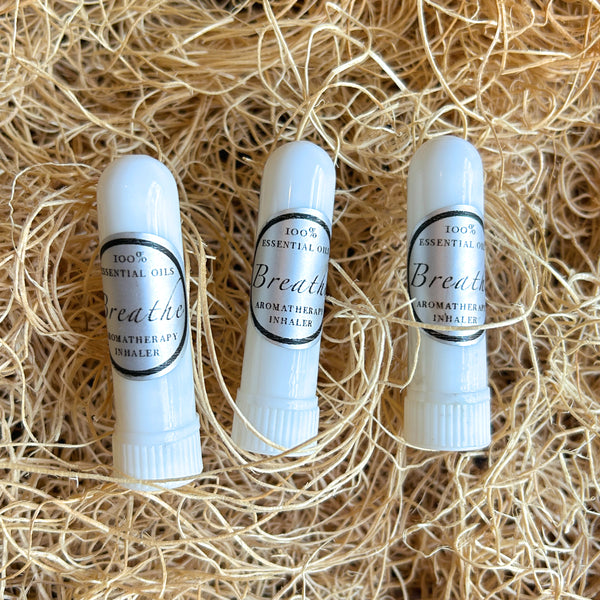 Three white lip balm tubes labeled 'Breathe Aromatherapy Inhaler' resting on a bed of light tan shredded paper.