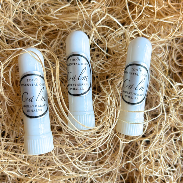 Three white essential oil spray bottles labeled 'Calm' by Calm Apothecary Inhaler, arranged on a bed of natural tan shredded paper.