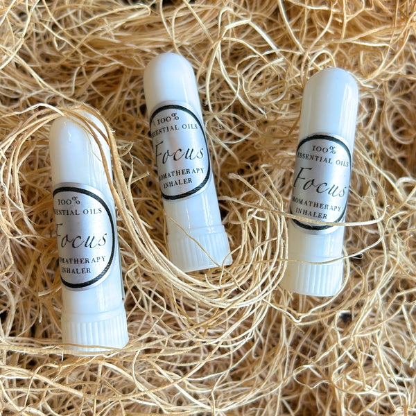 Three white essential oil inhaler tubes labeled 'Focus' by Weatherapy, arranged on a bed of light tan shredded paper.