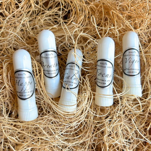 Five white essential oil lip balm tubes labeled with different scents (Haze, Breath, Calm, Focus, Vigor) arranged on a bed of natural tan shredded paper.