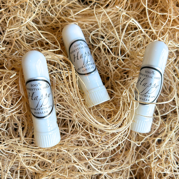 Three white essential oil inhaler sticks labeled 'Happy' resting on a bed of light tan shredded paper.