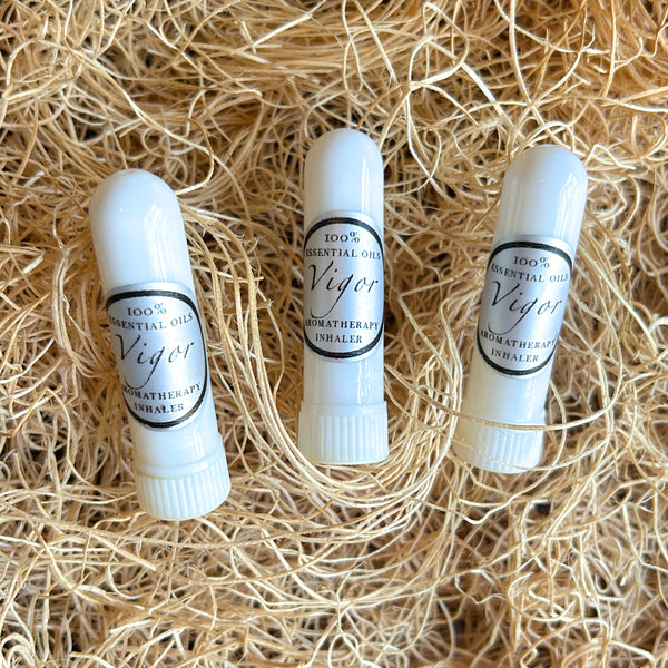 Three white lip balm tubes labeled '100% Essential Oils Viger Aromatherapy Inhaler' arranged on a bed of light tan shredded paper.